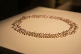 An ornate shell necklace sits on a lit surface.
