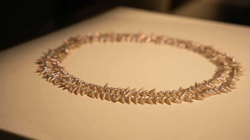 An ornate shell necklace sits on a lit surface.