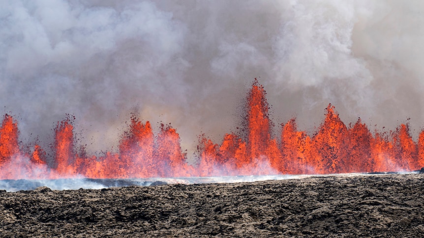 Bright orange lava erupts from the black ground as smoke pours into the sky