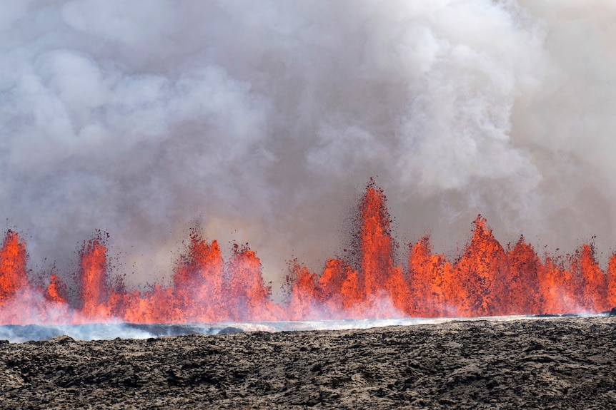 Bright orange lava erupts from the black ground as smoke pours into the sky