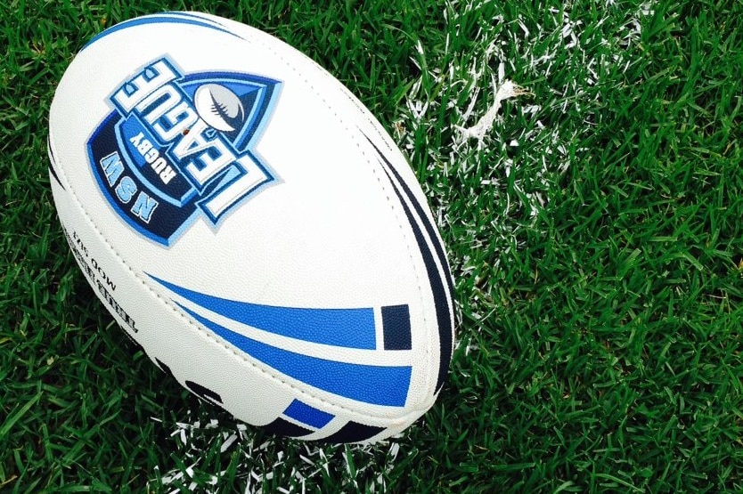 A white and blue rugby league ball lies on green grass with a white painted line.