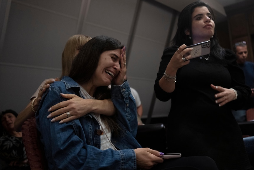 A woman holds her head in her hand as she openly sobbed, while another woman consoles her