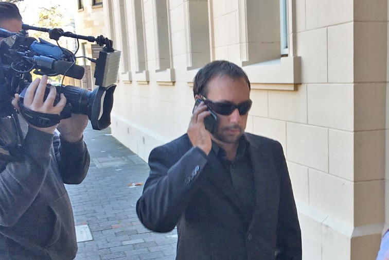 A man walks past a TV cameraman while talking on his mobile phone.