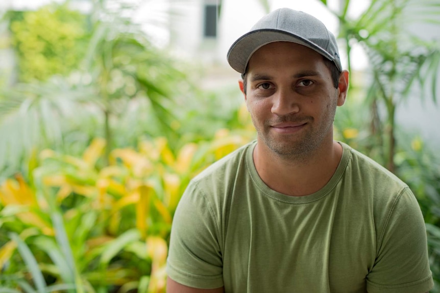 A young Indigenous man wearing a green t shirt and a cap smiles