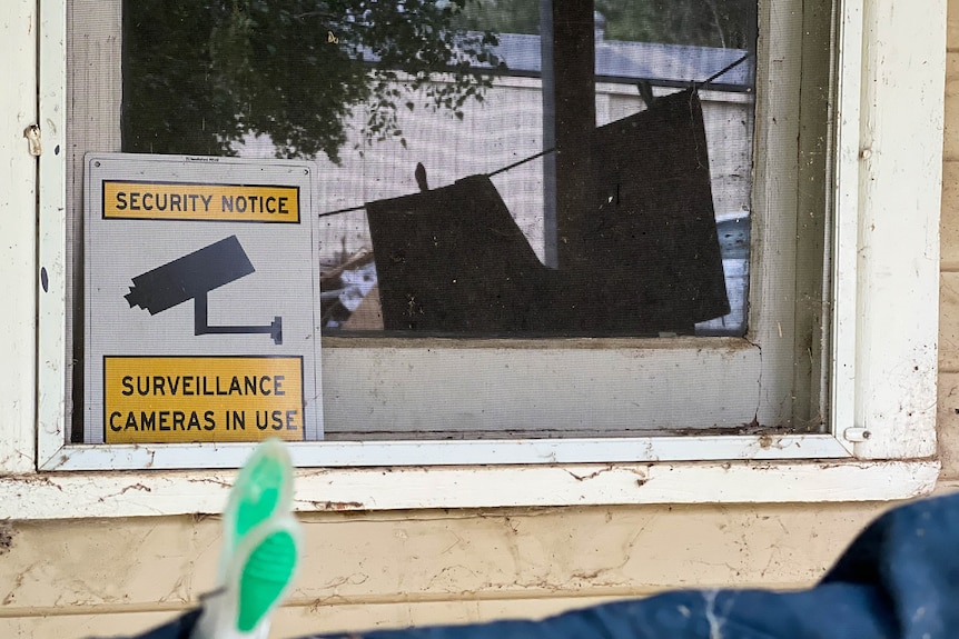 A window surrounded in cobwebs. A sign on it reads 'security notice, surveillance cameras in use.'