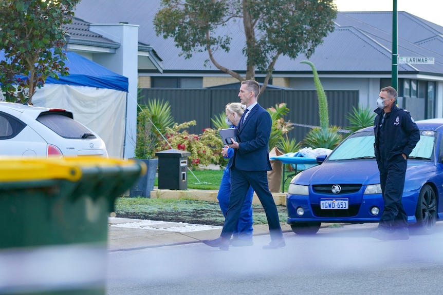 A suited man and a police officer in blue overalls appraoch a house with blurred police tape and a bin in the foreground