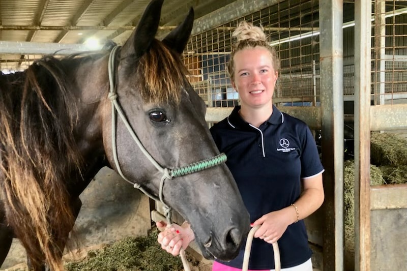 Young woman stands in stables with a chestnut horse