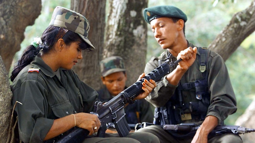 FARC troop supervises a fighter as she cleans her gun