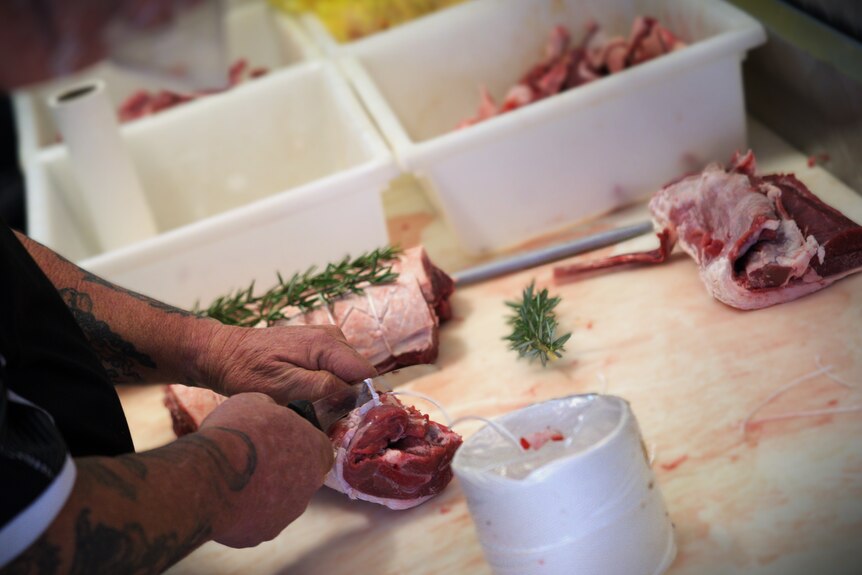 Arm of a butcher cutting and tying meat with rosemary on a table