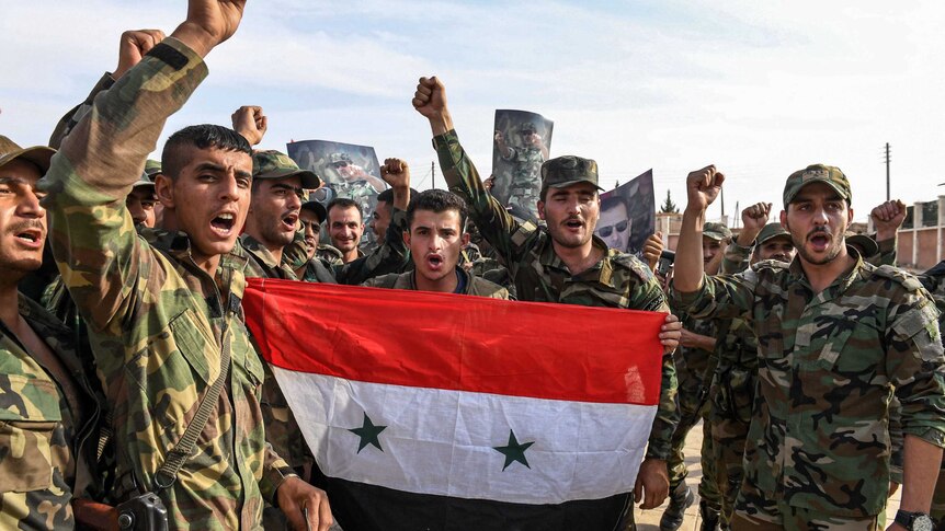 Syrian government soldiers chant slogans as they pose for a group photo with a national flag outside Manbij.