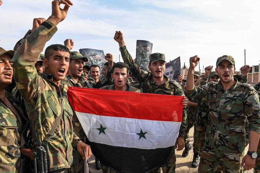 Syrian government soldiers chant slogans as they pose for a group photo with a national flag outside Manbij.