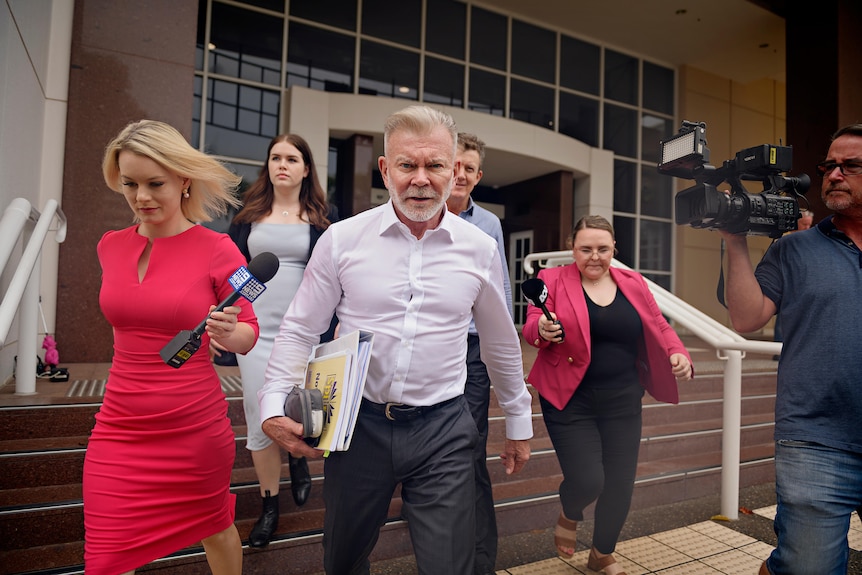 A man with a serious expression walks down the steps of a courtroom.