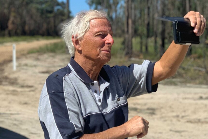 Garry Squires uses his phone to take a photo of a forest burnt by fire.