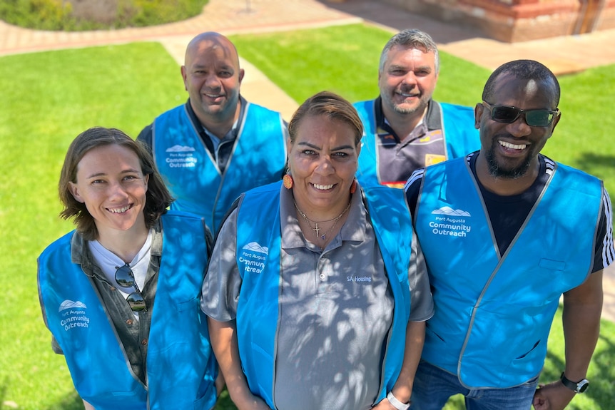 Five members of the Outreach team stand together at the Fountain Gallery wearing blue Outreach Team vests