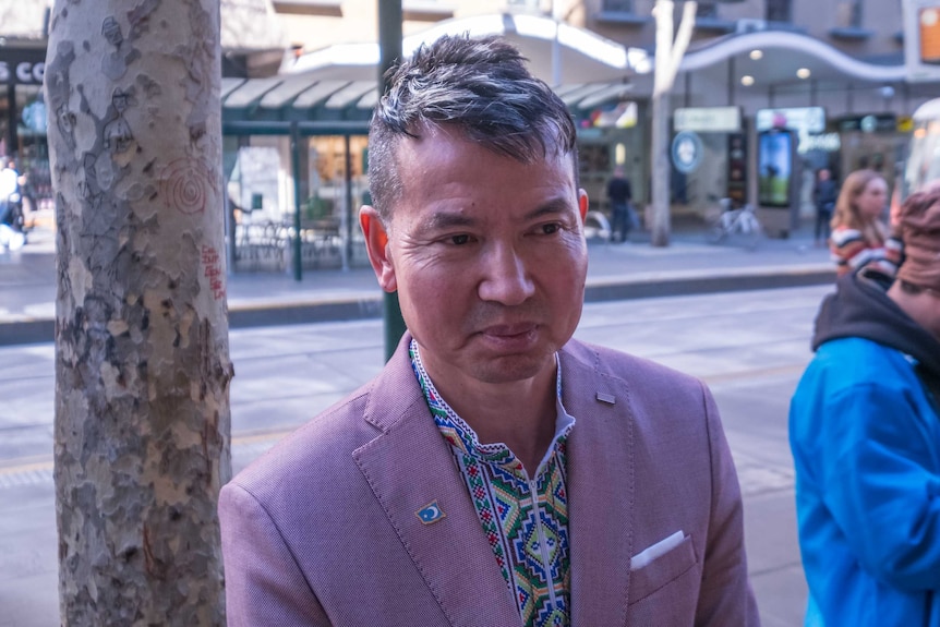 A Uyghur man wearing a traditional colourful stitched shirt and pink blazer with a Uyghur flag pin.