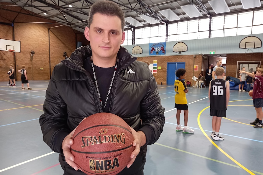 James holds a basketball, players behind him on the court.