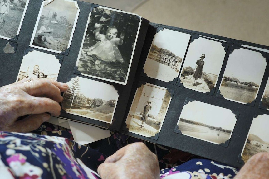 A pair of hands holds open a photo album filled with black and white images.