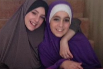 Two girls sit side by side smiling at the camera.