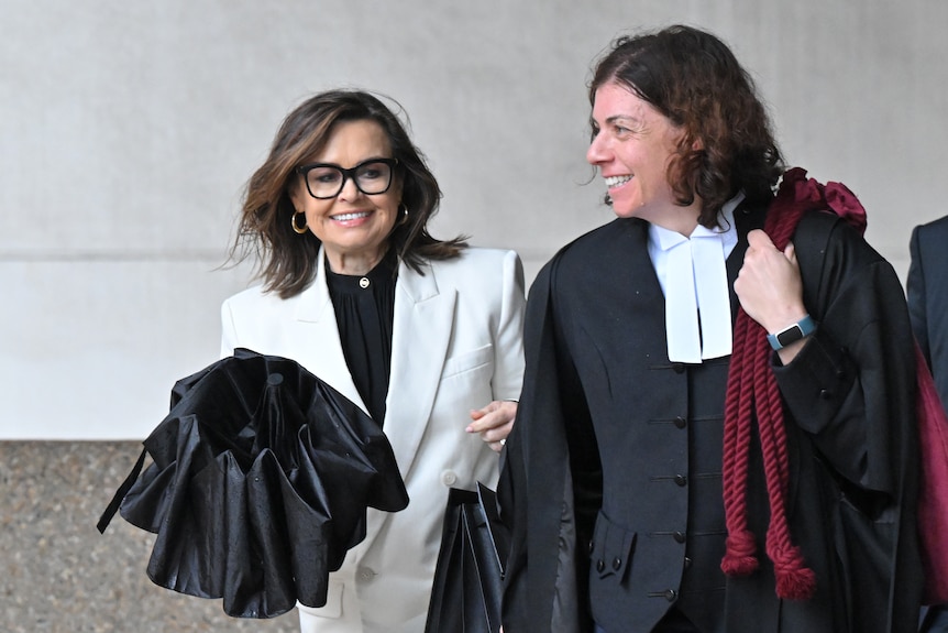 A woman in a white suit jacket and a woman in barristers clothes walk together.