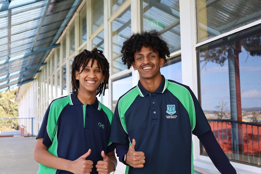 Two boys wearing school sports uniform give a thumbs up and smile