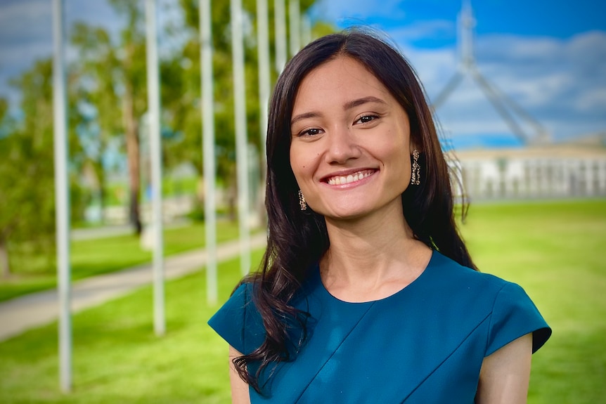 Yasmin Poole, a woman with dark brown hair, poses for a photo in front of the lawns of Parliament House Canberra