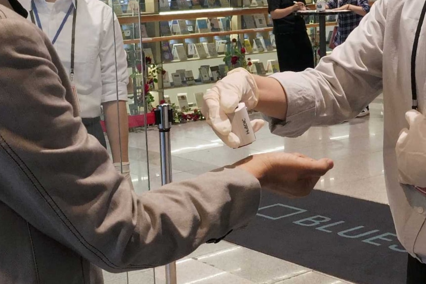 Two men stand at door to shop. On offers the other hand sanitiser.