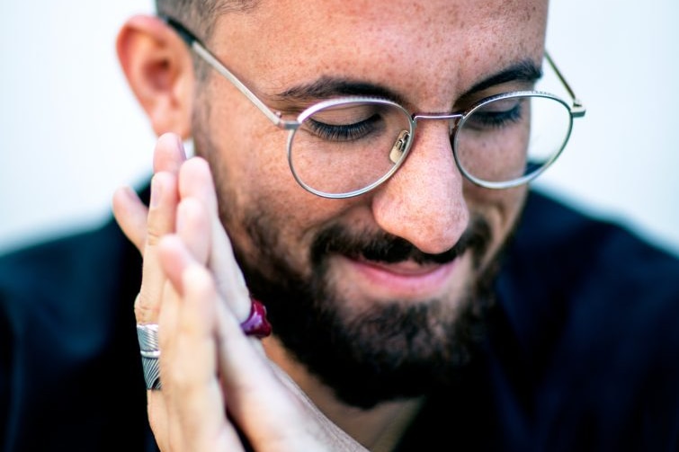 Pianist Igor Levit smiling and looking down with his hands clasped together.