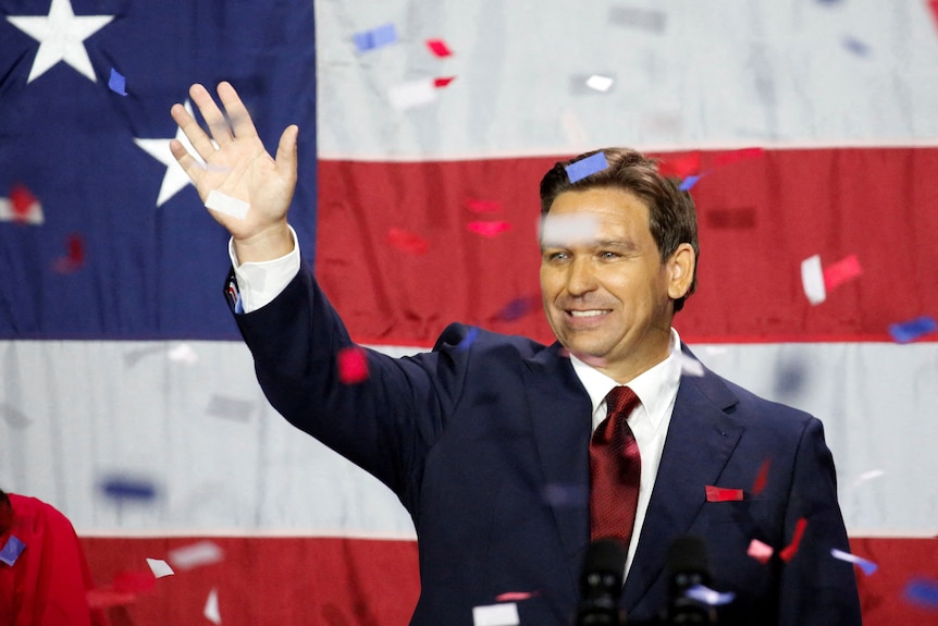 Ron DeSantis waves at a crowd while confetti rains down in front of a US flag