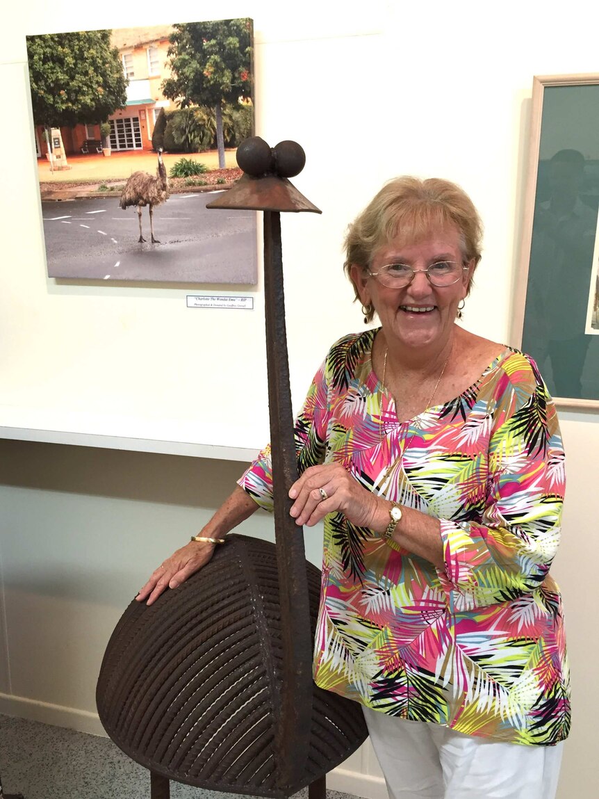 Elaine Madill stands beside a metal sculpture of an emu that is as tall as she is