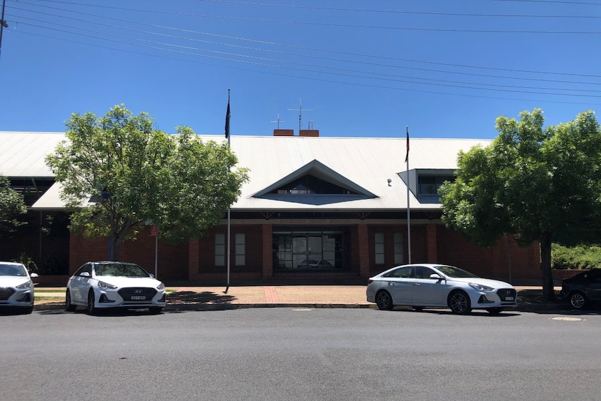 A brick building with a tin roof and a sign reading Bathurst Police Station. Several cars are parked out the front.