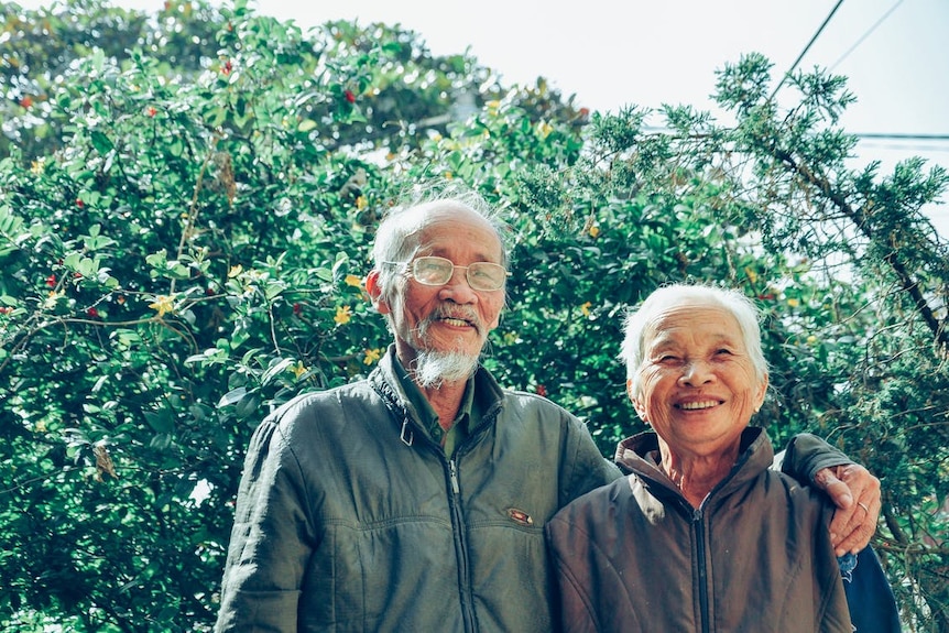 Older heterosexual couple in nature, the man has his arms over the woman's shoulder, they are smiling