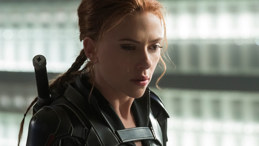 Close-up of Scarlett Johansson looking concerned, wearing a black superhero suit, with a weapon strapped to her back