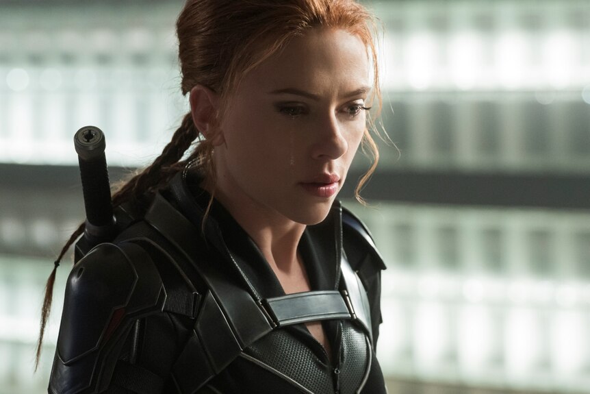 Close-up of Scarlett Johansson looking concerned, wearing a black superhero suit, with a weapon strapped to her back