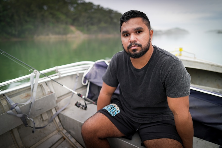 Leeroy sits in a boat on the water, looking into the camera with a serious expression.