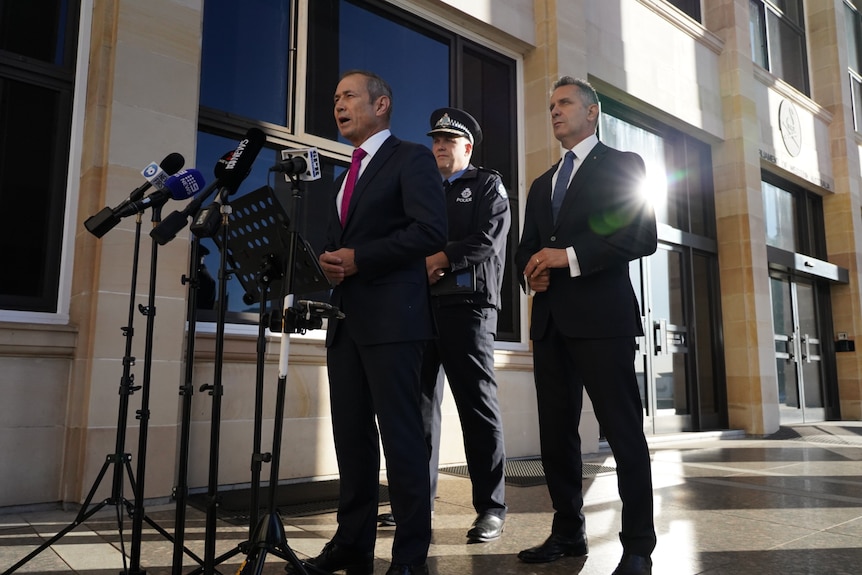 Roger Cook speaks into microphones at a media conference outside parliament, flanked by Col Blanch and Paul Papalia.