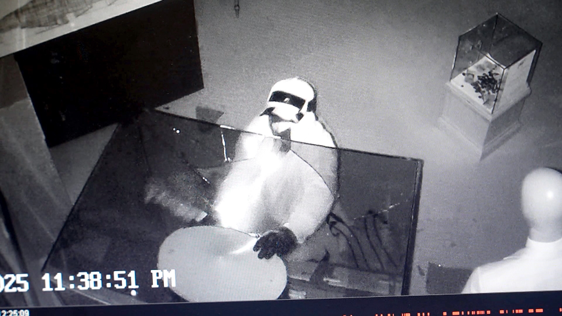 Un ladrón con una sudadera con capucha brillante mete la mano en una vitrina rota.