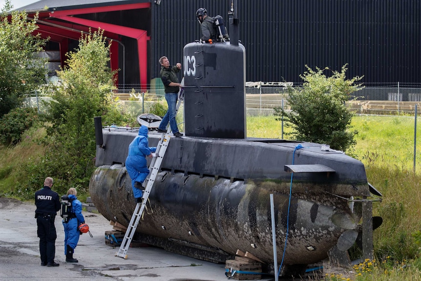 Wide shot of police inspecting a submarine on dry land.