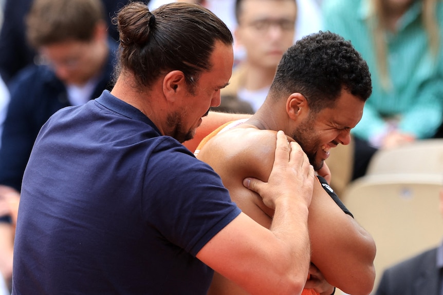 A tennis player winces as a physio treats his shoulder.