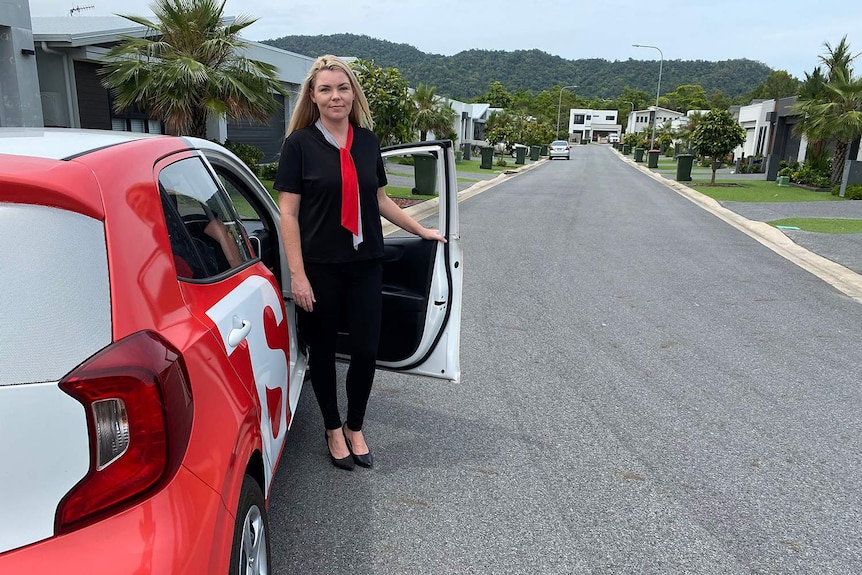 Cairns real estate agent Nicole Craike stands beside her car in a street with new houses.