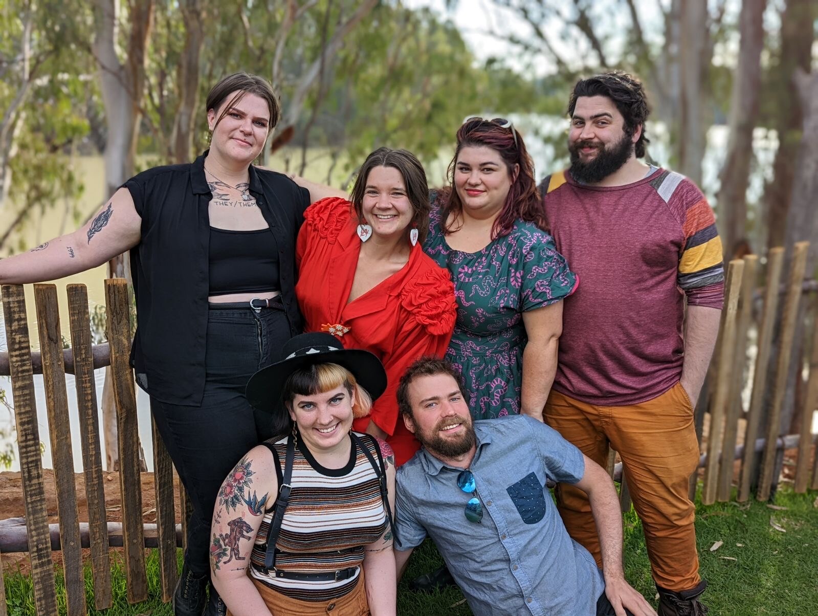 Six people stand in front of a fence with a wide river in the background. 