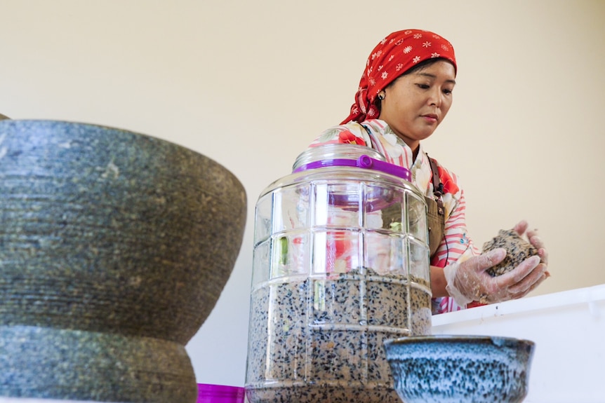 A woman wearing traditional Japanese clothing mixing soya beans and rice to make miso.