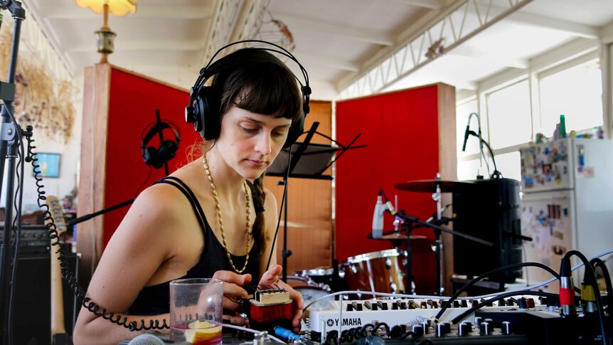 Erica Dunn wears headphones, focussed on a keyboard inside a studio room.
