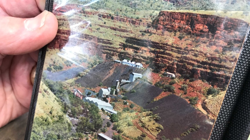 Closeup of a photo in a photo album of an open cut mine with steep red dirt cliffs.