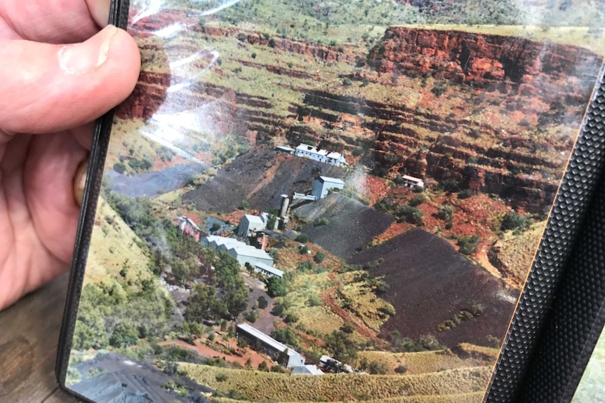 Closeup of a photo in a photo album of an open cut mine with steep red dirt cliffs.