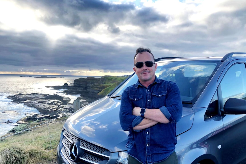 Tour operator Simon Greenland leaning on his car parked near a beach at Phillip Island
