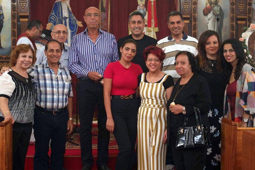 A group of men and women stand inside a Coptic Orthodox church, smiling.