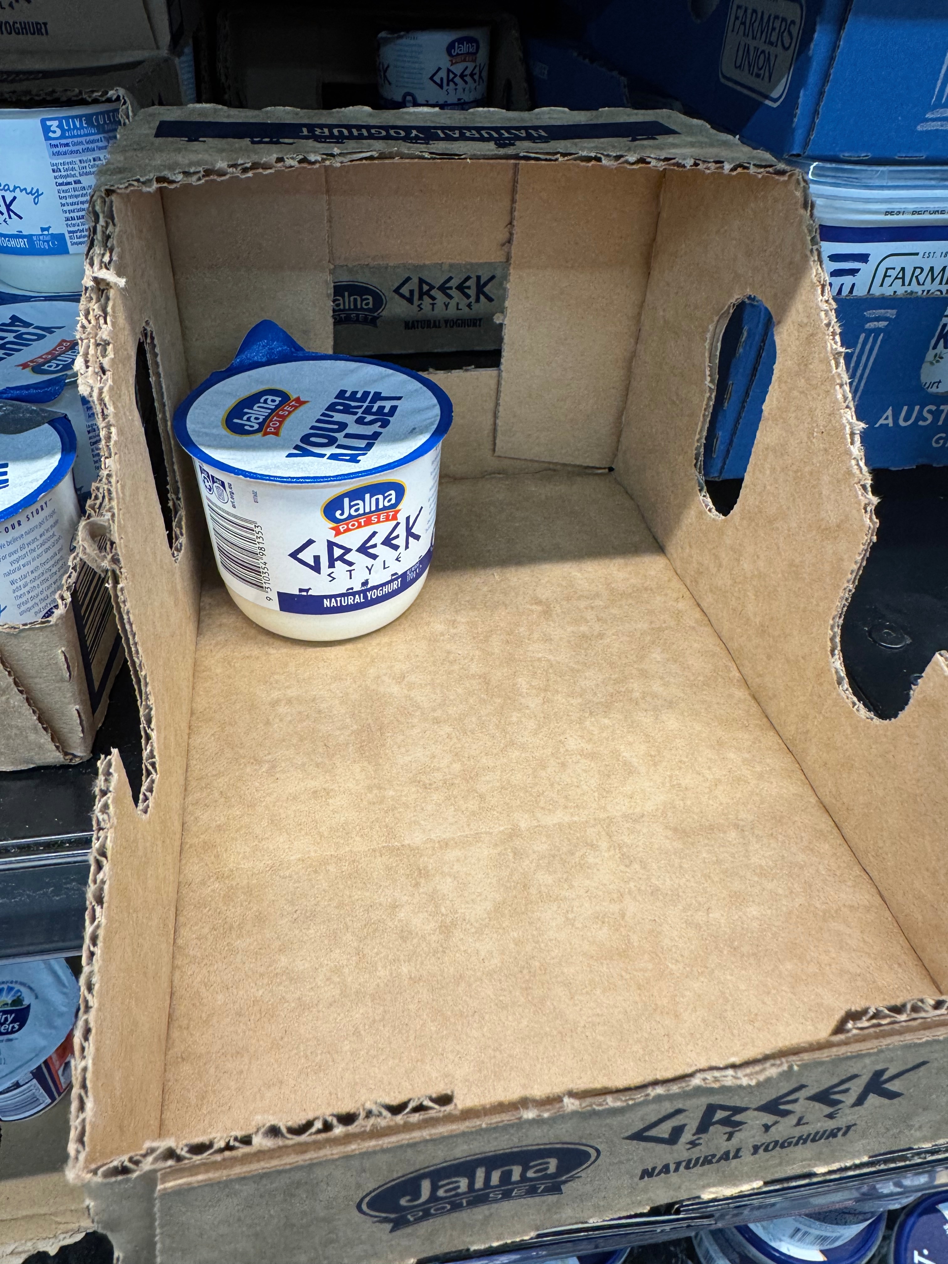 A blue and white coloured tub of Greek yoghurt in a supermarket fridge.