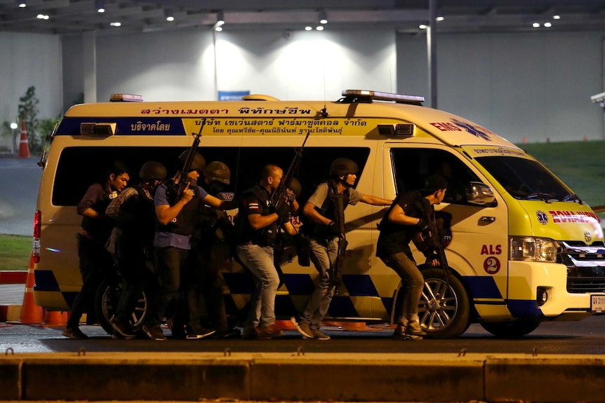 A group of guards with guns huddle behind an ambulance in an active shooter situation.