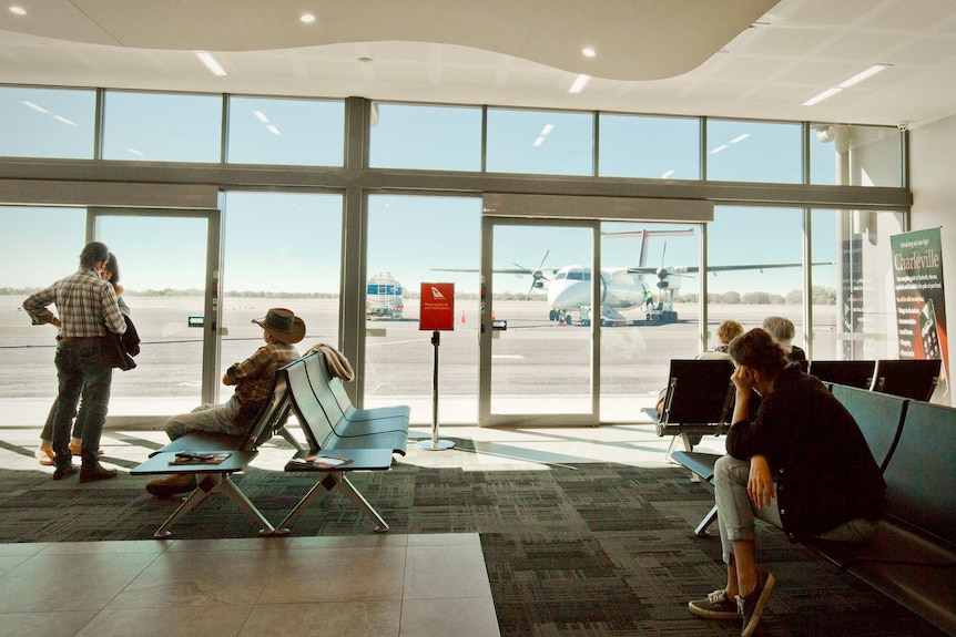 Taken from inside the terminal, passengers look out to a plane on the tarmac.