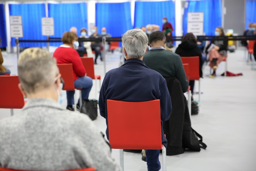 People seated in chairs waiting for a COVID vaccine